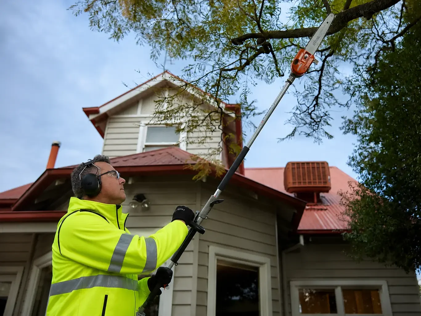 COMSTRA Mowing gardener pruning a tree with a pole saw at a commercial property in Essendon